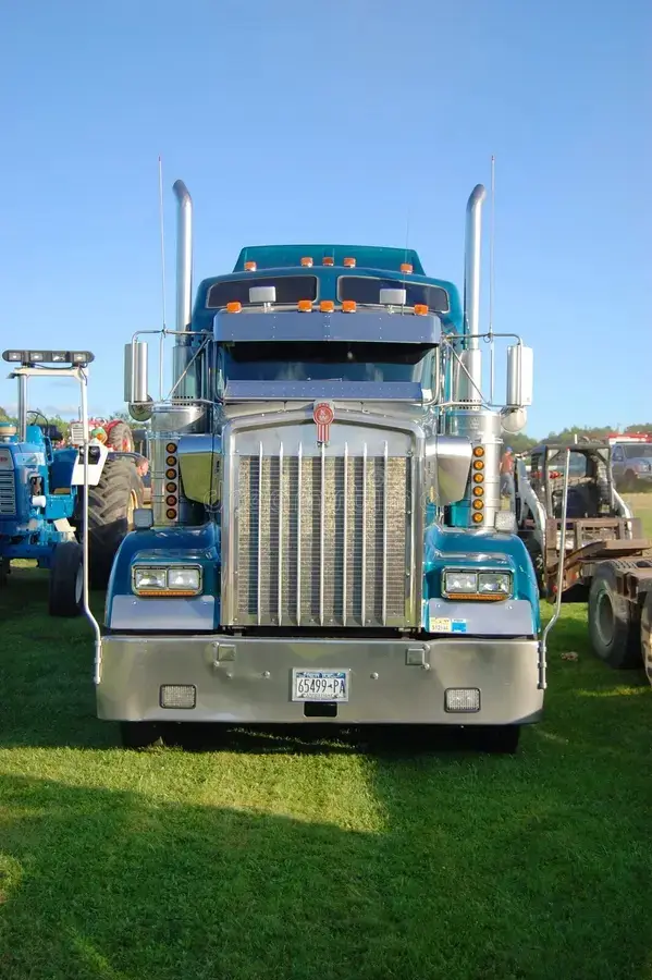A large, shiny blue Kenworth semi-truck with chrome accents and Pennsylvania license plate is parked on grass at an outdoor…