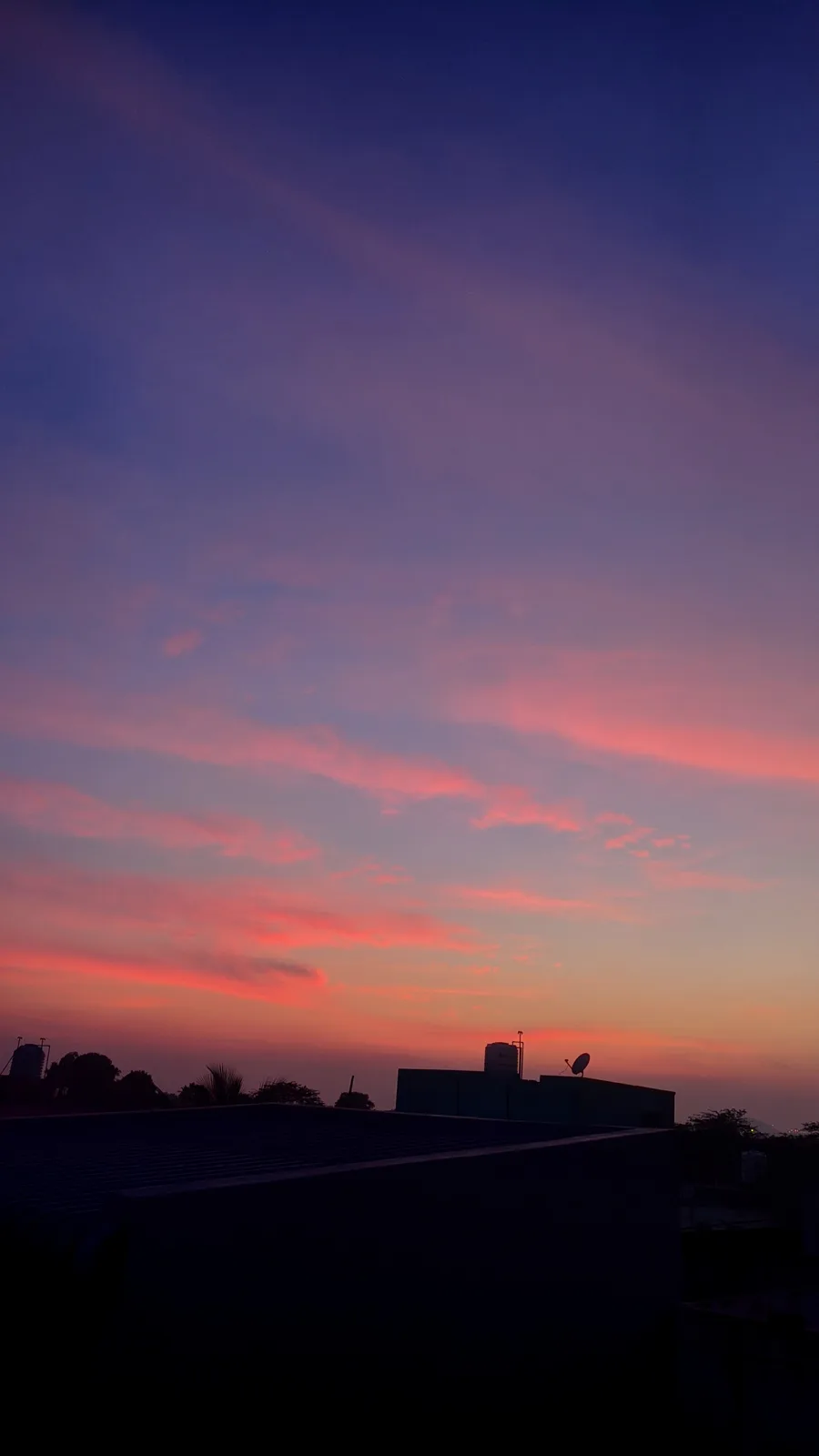 A photograph of a vibrant sunset or sunrise with pink, orange, and purple clouds against a darkening blue sky, silhouetting…