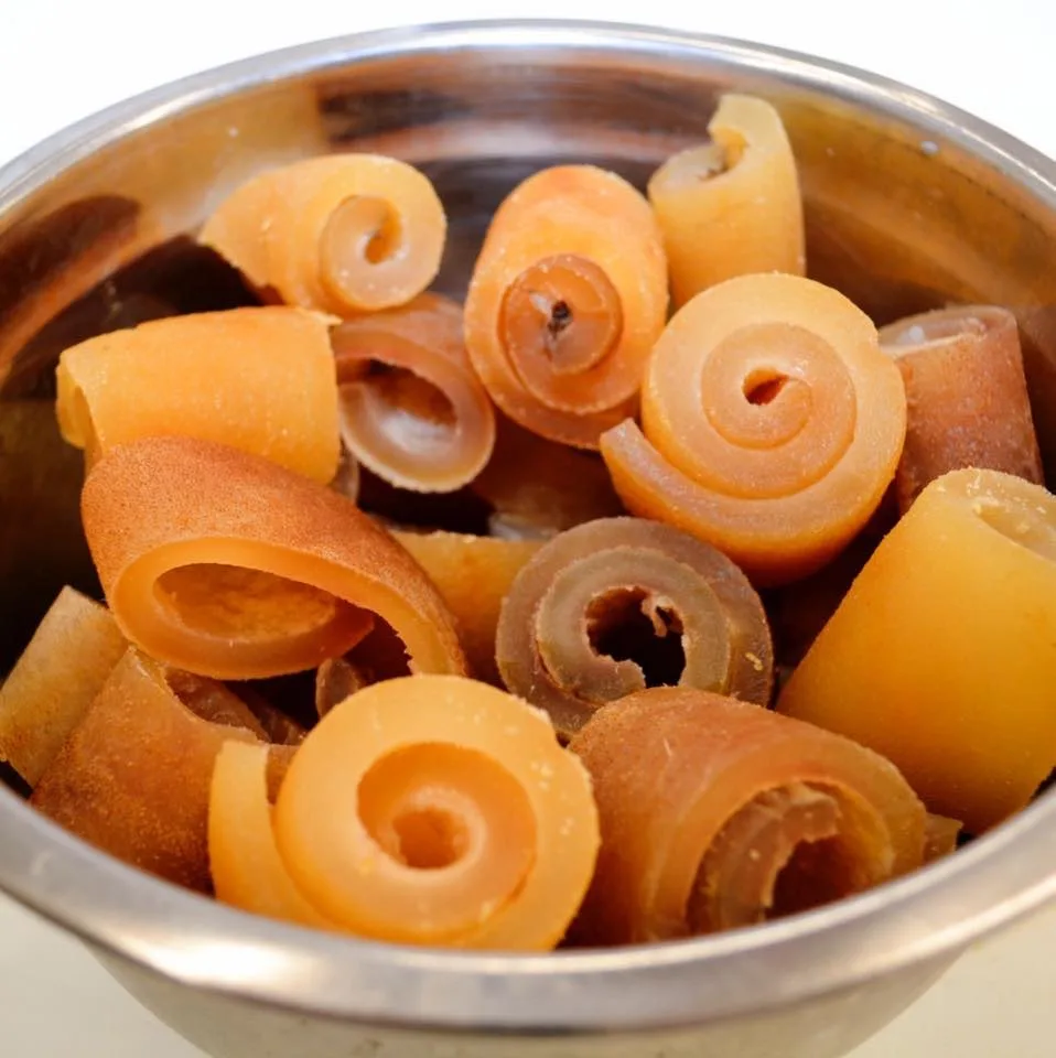 a close-up photo shows a metal bowl filled with spiral-shaped, translucent orange-yellow rolls that resemble candy or jerky…