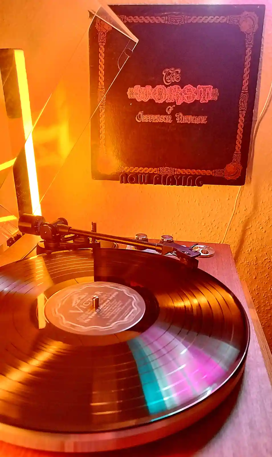 A vinyl record spins on a turntable under warm orange lighting, with its album cover visible behind it. The cover reads 'The…