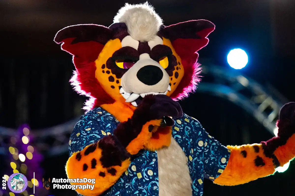 A person in a detailed fursuit resembling a spotted feline with red and orange fur, dark markings, and a white tuft on top…