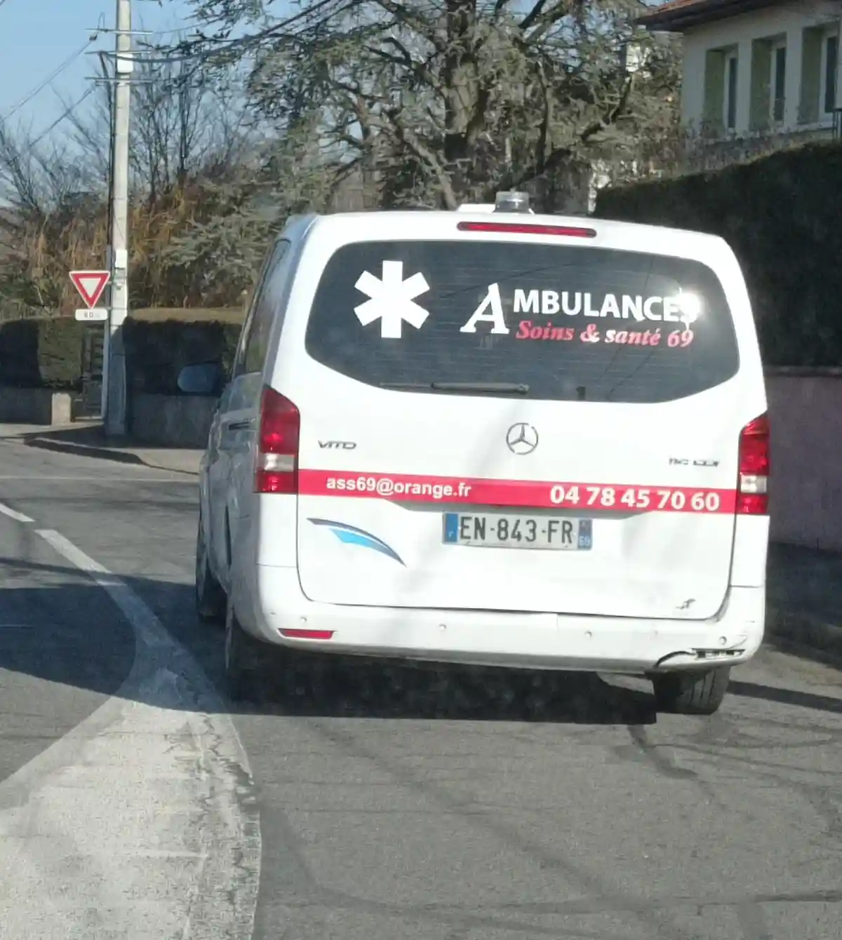 The back of a white Mercedes-Benz Vito van, marked as an ambulance with a star of life symbol and text 'AMBULANCES Soins &…