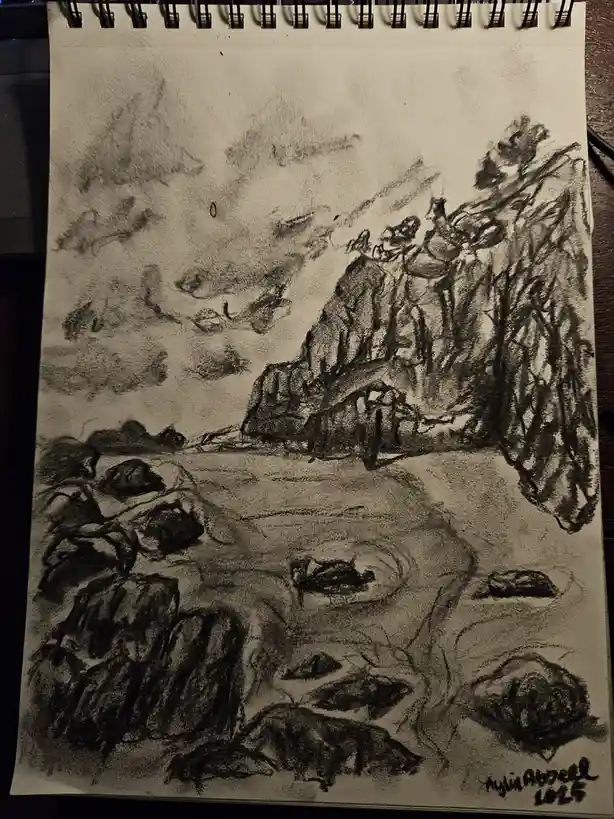 A black-and-white charcoal sketch on spiral-bound paper depicts a rocky coastal scene with cliffs, scattered boulders, and…