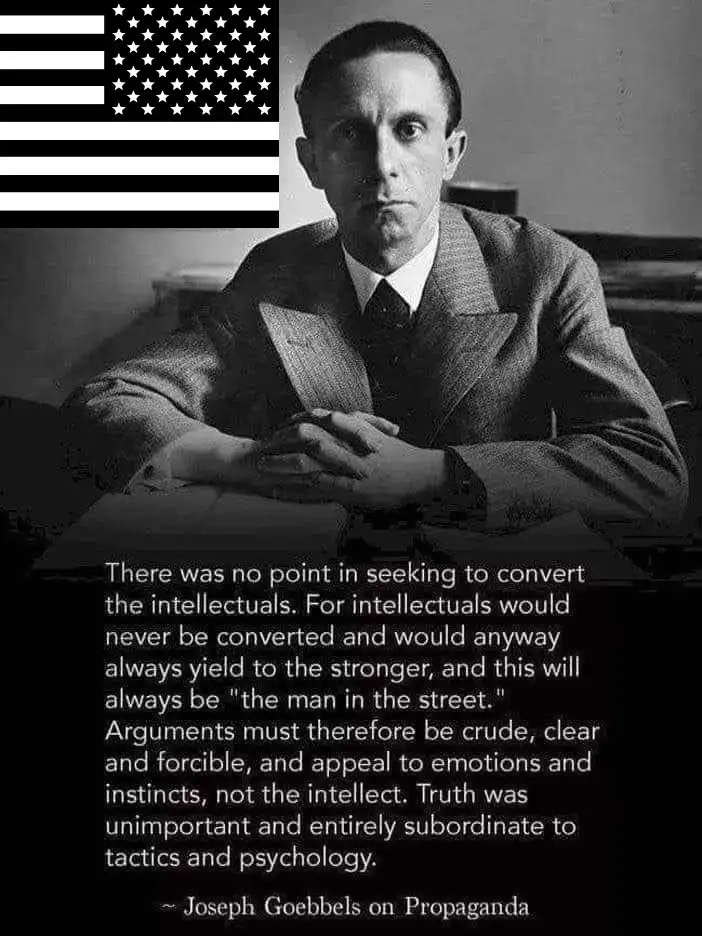 A black-and-white photo of Joseph Goebbels seated at a desk with an American flag in the top-left corner. Overlaid text…