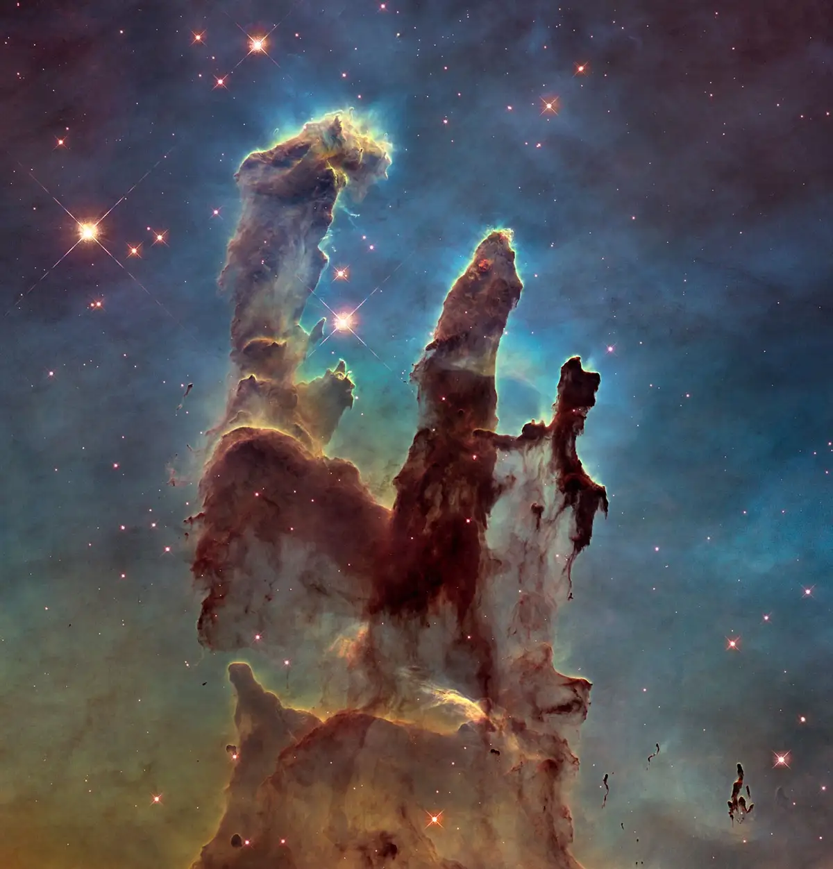 A cosmic image of the Pillars of Creation in the Eagle Nebula, showing towering columns of gas and dust illuminated by…
