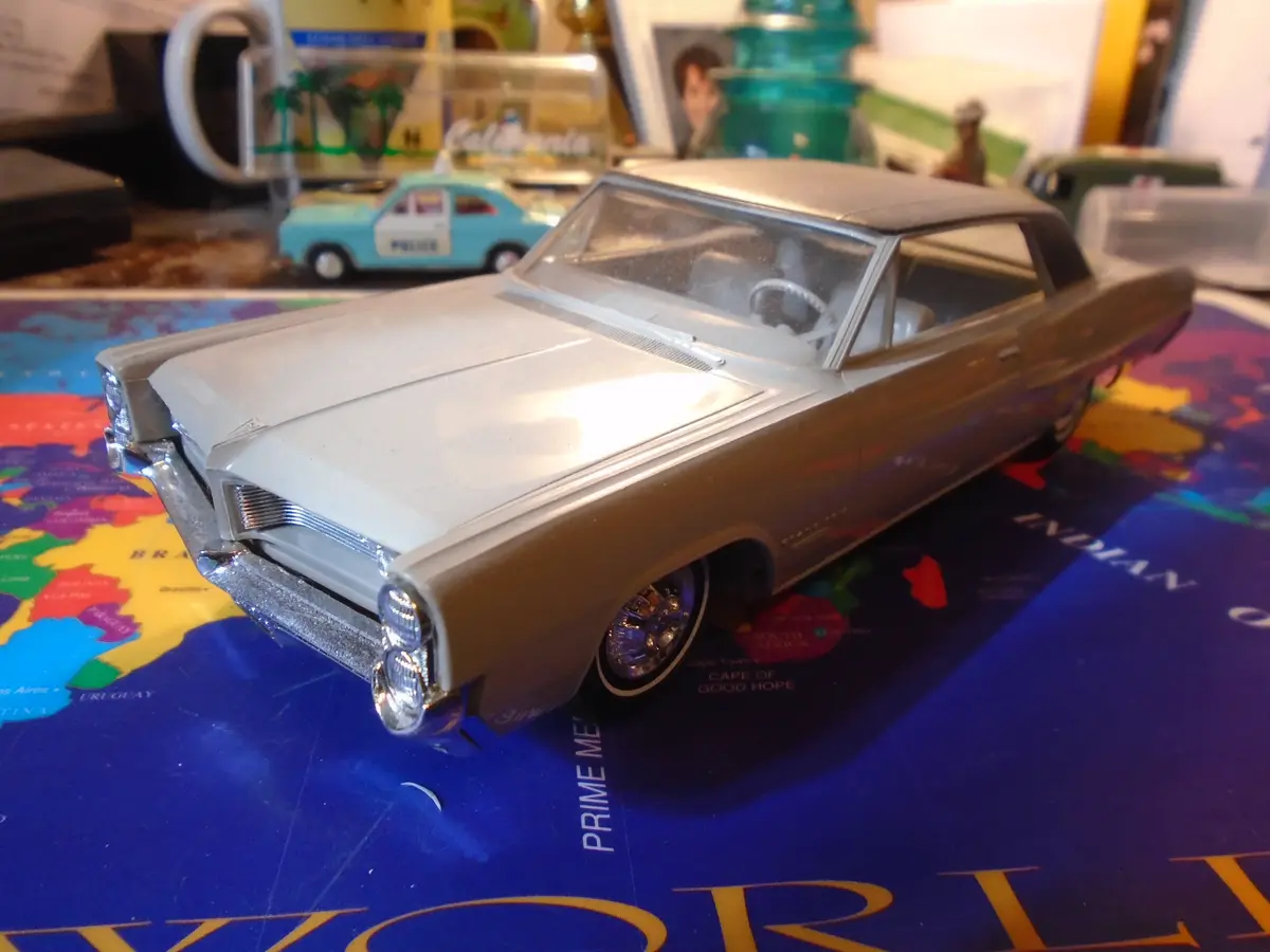 A silver die-cast model of a classic American car, likely a 1960s Pontiac, sits prominently on a colorful world map. The car…