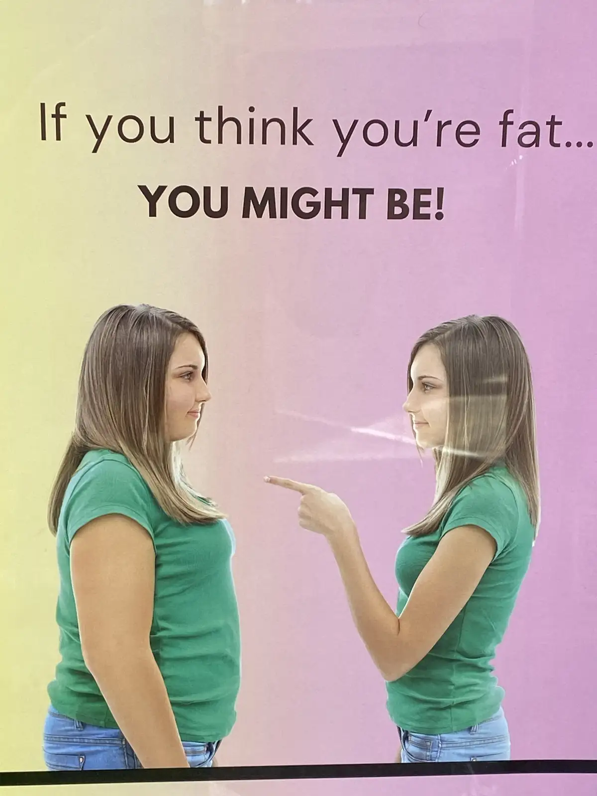 A promotional poster shows a woman in a green t-shirt and jeans standing in front of a mirror, pointing at her reflection…