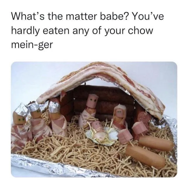 A food art nativity scene made from bacon, hot dogs, and chow mein noodles on a foil-lined tray. The 'stable' is formed by…