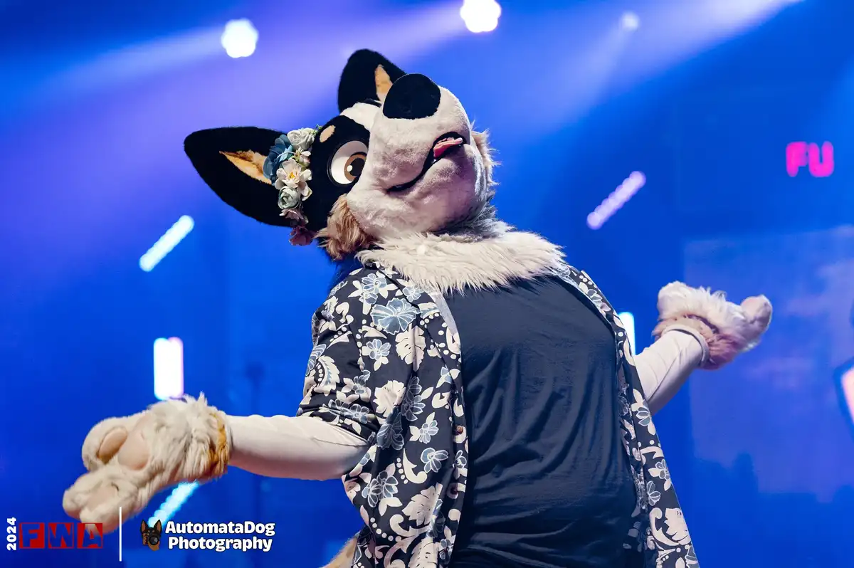 A person in a detailed black-and-white dog fursuit with a floral crown on their head is captured mid-performance on a…