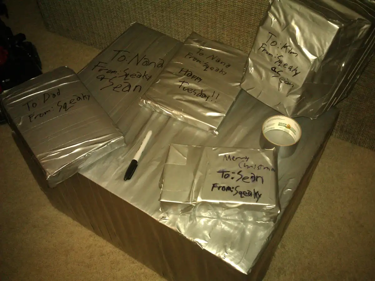 Several packages wrapped in silver duct tape sit on a carpeted floor, each labeled with handwritten messages like 'To: Dad…