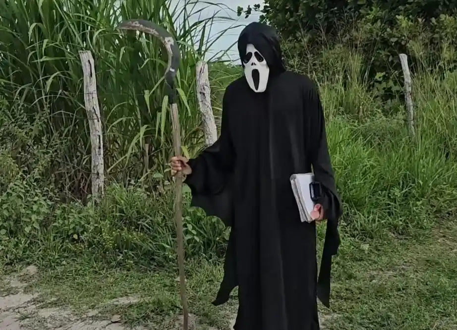 A person dressed as the Ghostface killer from 'Scream', wearing a white mask with black eye and mouth holes, a black hooded…
