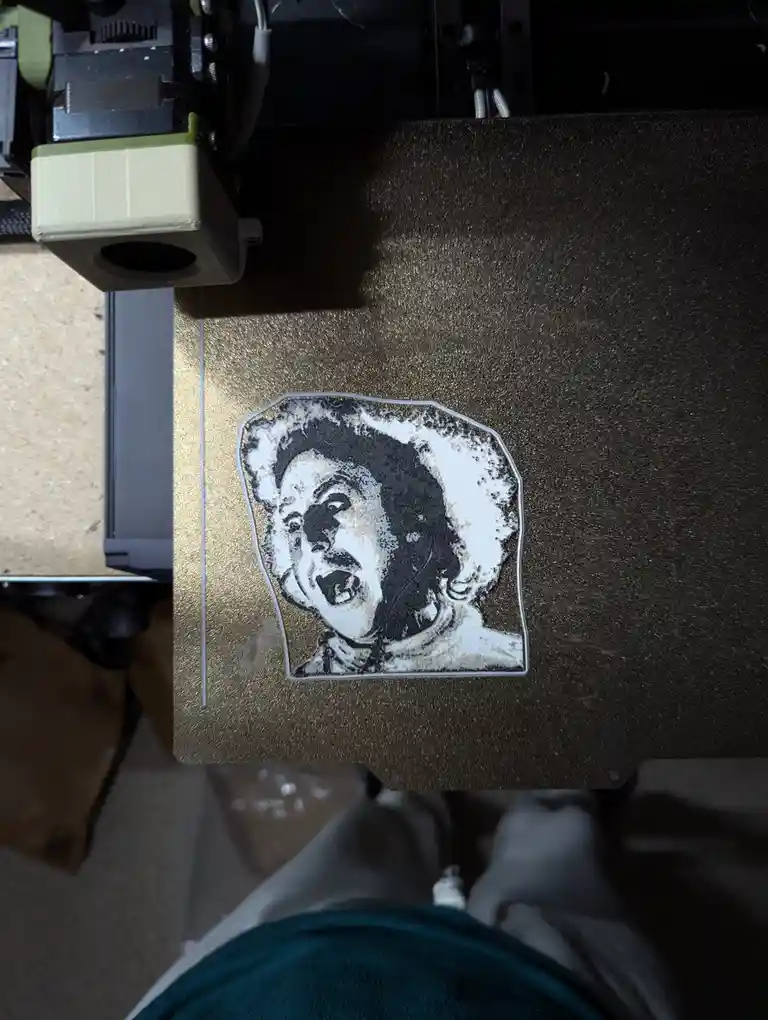 A 3D printer's print bed displays a crudely rendered, black-and-white portrait of a person with an exaggerated, screaming…
