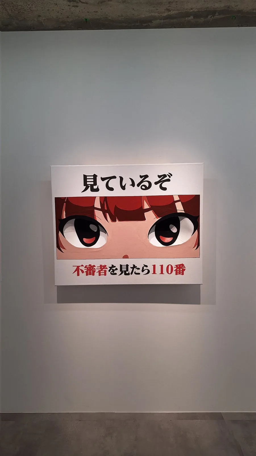 A framed artwork on a gallery wall displays a close-up of an anime-style character's face with large, expressive eyes. The…
