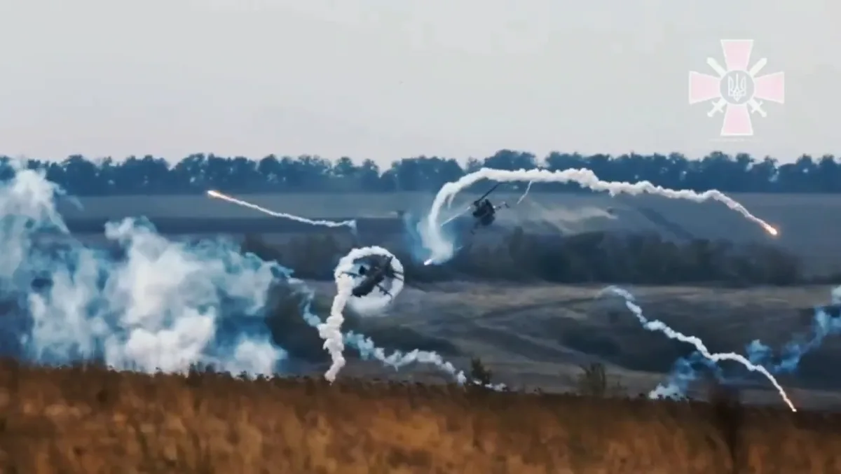 Two military helicopters are shown flying low over a field, emitting smoke trails and firing missiles, with a pink cross…
