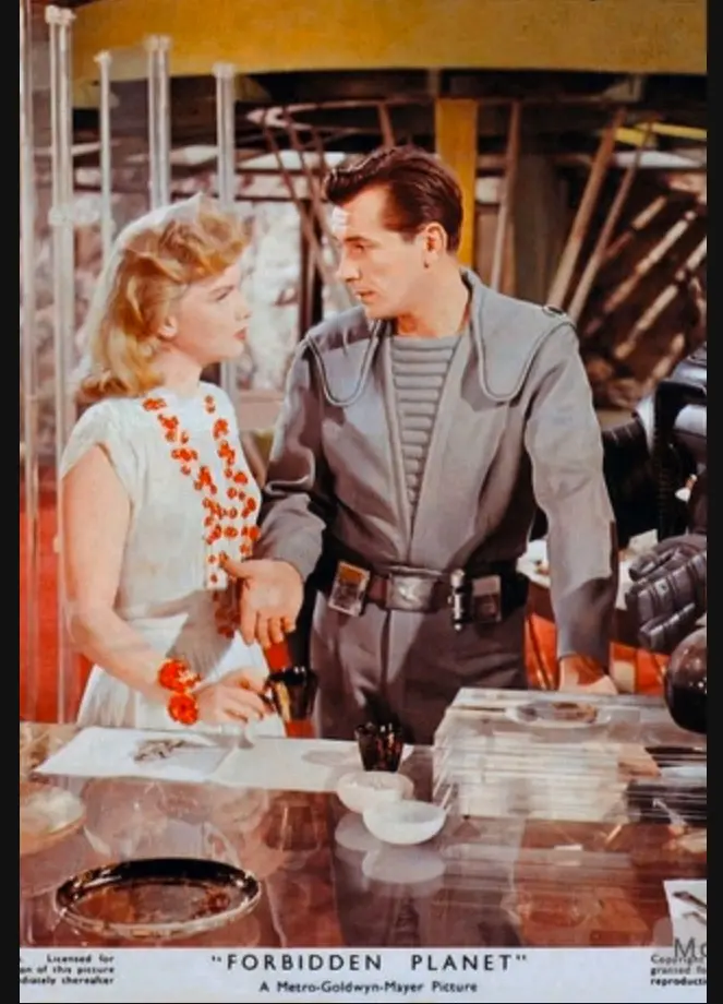 A vintage promotional still from the 1956 sci-fi film 'Forbidden Planet' shows a man in a grey futuristic uniform and a…