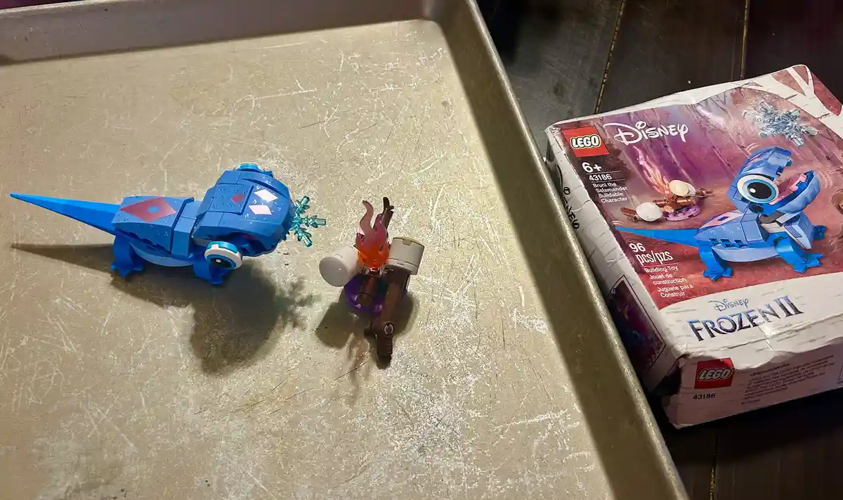 A LEGO Disney Frozen II set (43186) featuring Brun the Salamander is shown next to its assembled blue salamander figure and…