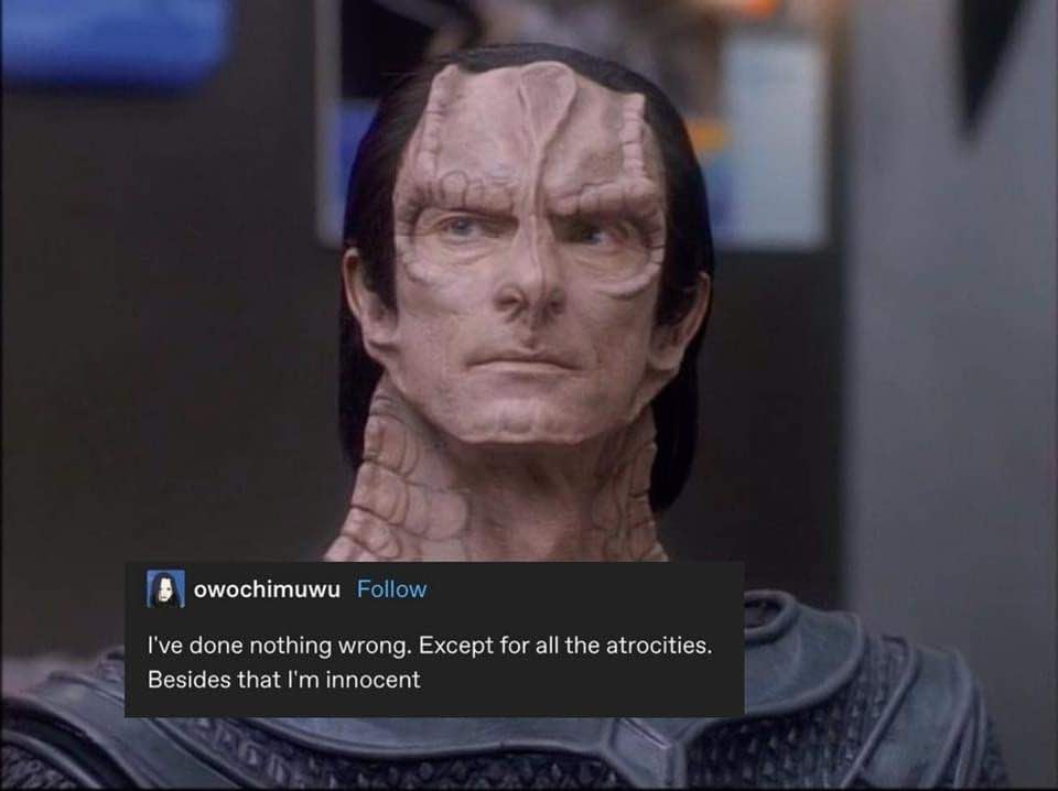 A close-up of a character with a reptilian, textured face and long dark hair, wearing armor, looking upward with a serious…