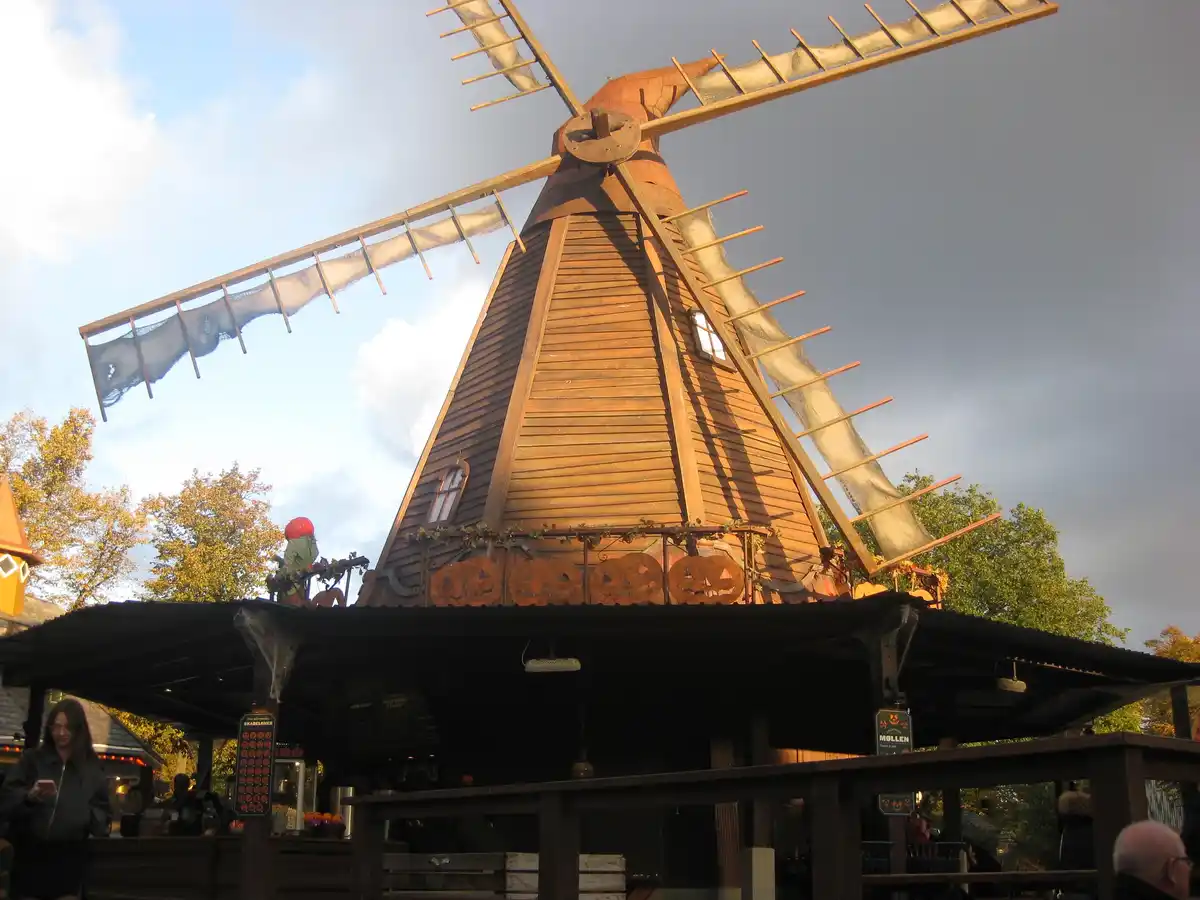 A wooden windmill decorated with Halloween jack-o'-lanterns and spiderwebs, with a person in a red hat on its roof and…