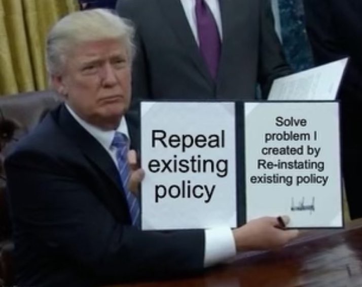 A man in a suit sits at a desk holding two signs. The left sign reads 'Repeal existing policy'. The right sign reads 'Solve…