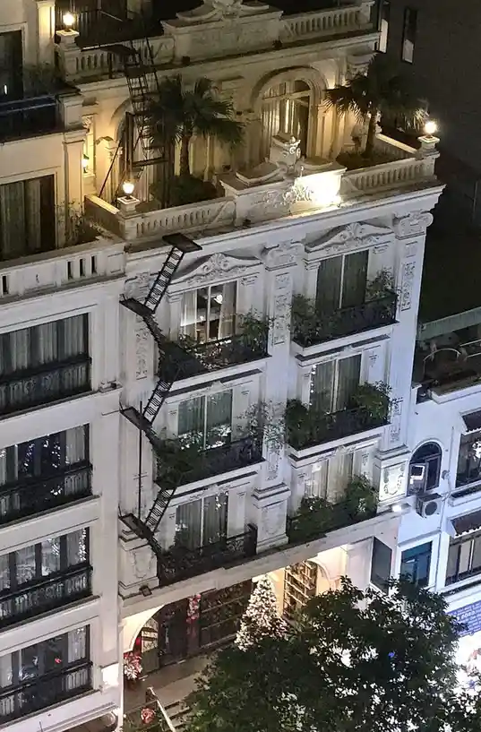 A nighttime photo of an ornate, multi-story white building with intricate architectural details and balconies. A black metal…