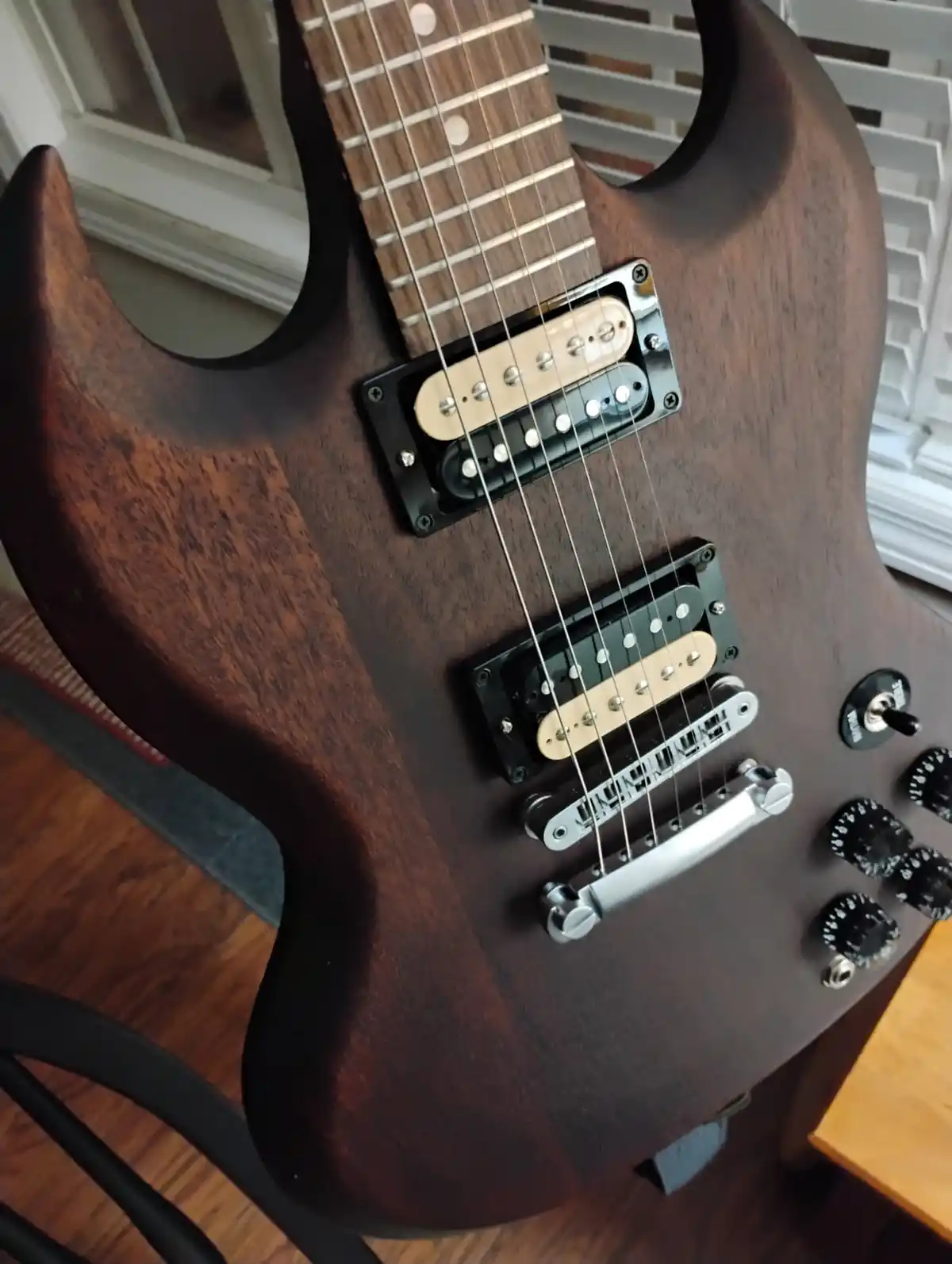 A close-up photo of a dark wood-finish electric guitar with two humbucker pickups, chrome hardware, and control knobs…