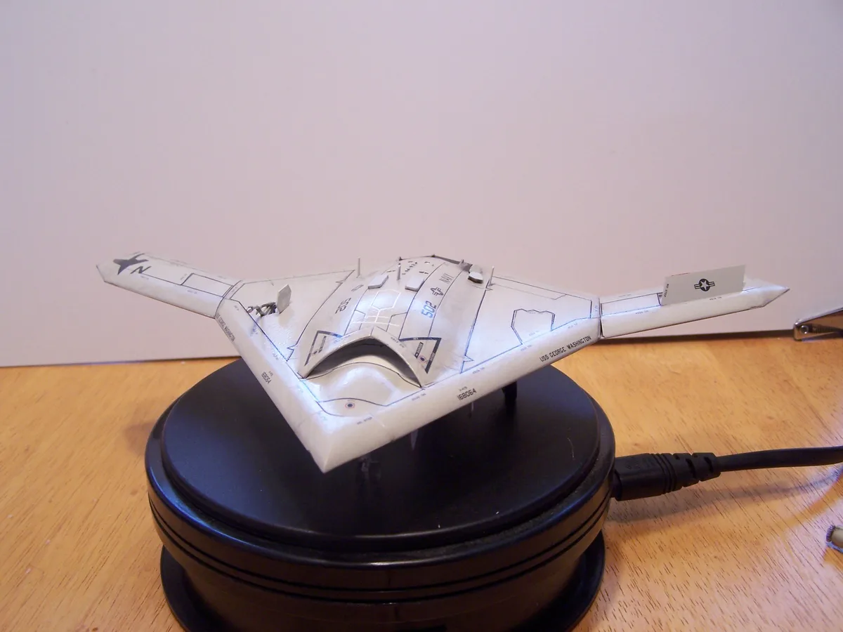 A model of a stealth fighter jet, resembling the B-2 Spirit, is displayed on a black USB hub, with a USB cable plugged into…