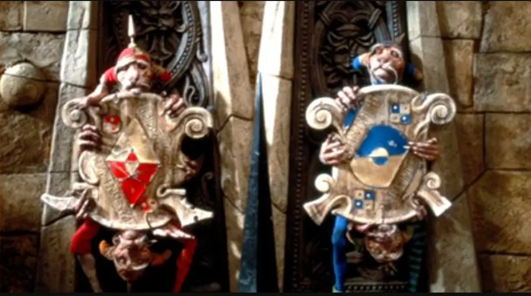 Two stone statues of medieval knights holding ornate shields stand side by side against a stone wall. The knight on the left…