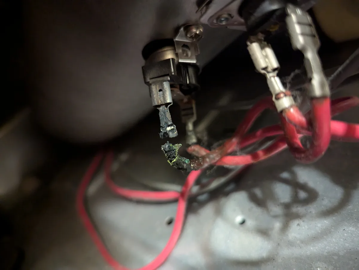 A close-up photo shows severely burnt and melted electrical wires and connectors inside a vehicle's engine bay, with charred…