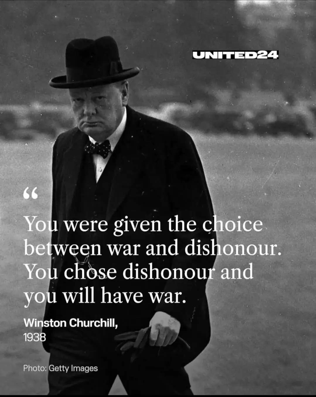A black-and-white photo of Winston Churchill wearing a suit, bow tie, and fedora, looking sternly forward while holding…