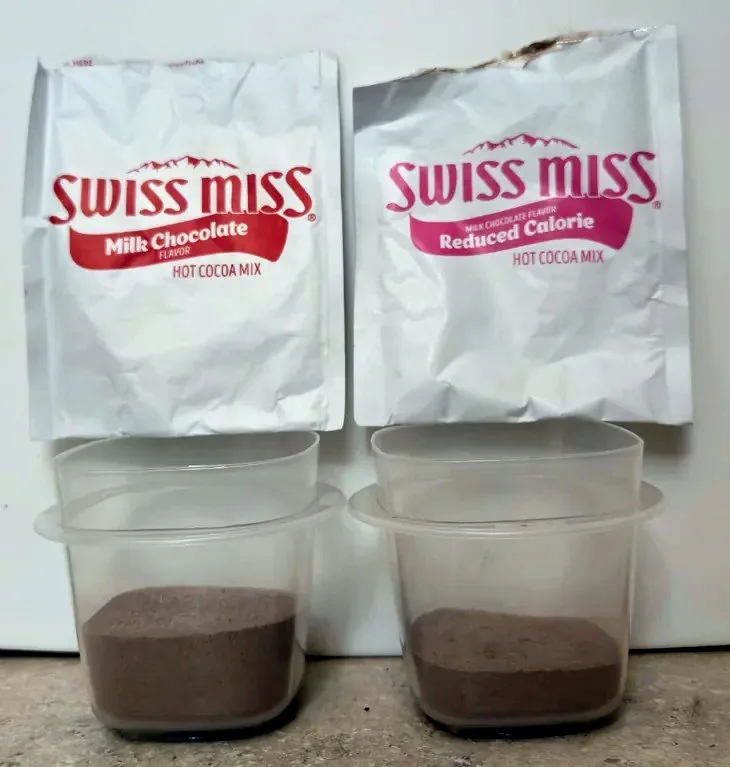 Two bags of Swiss Miss hot cocoa mix, one labeled 'Milk Chocolate Flavor' and the other 'Reduced Calorie', are positioned…