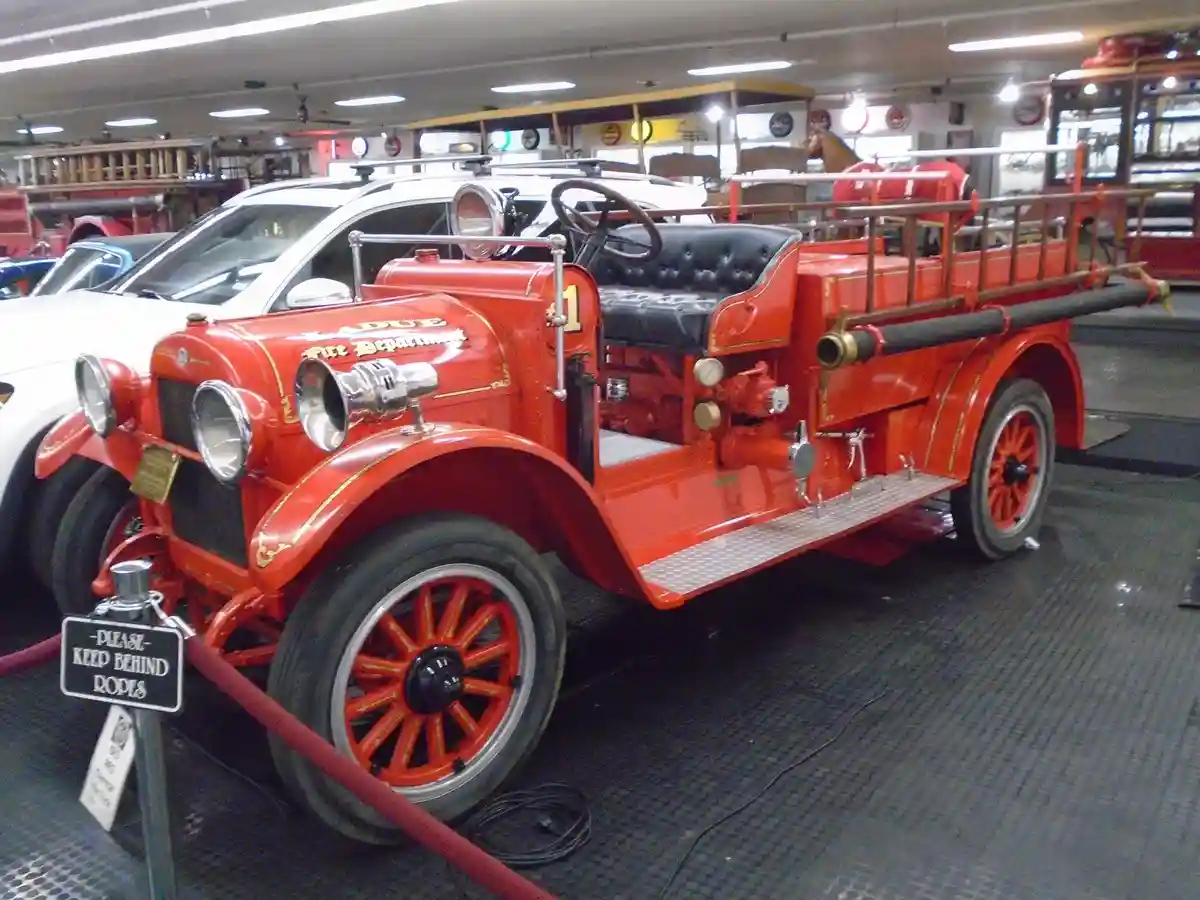 A vintage red Ladue Fire Department fire engine is displayed indoors behind a red rope barrier with a sign that reads…