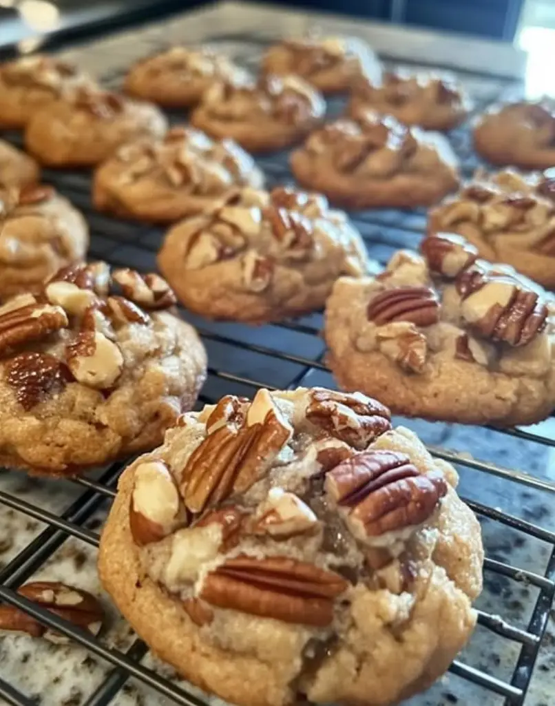 a close-up photo of freshly baked pecan cookies cooling on a wire rack, with visible golden-brown cookies topped with whole…