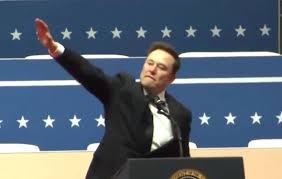 elon musk stands at a podium with a blue wall of white stars behind him, raising his right arm in a gesture resembling a…