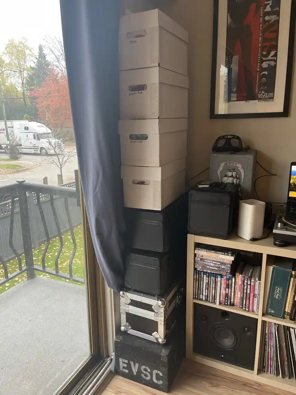 A room corner shows a tall stack of white storage boxes, black cases, and a large black case labeled 'EVSC' at the base…