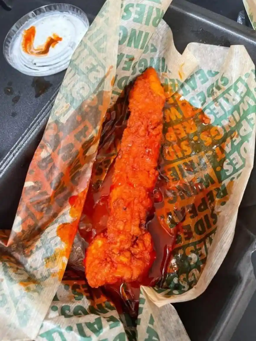 A close-up photo shows a single, heavily sauced fried chicken wing resting on branded paper that reads 'SIDE OF WINGS…