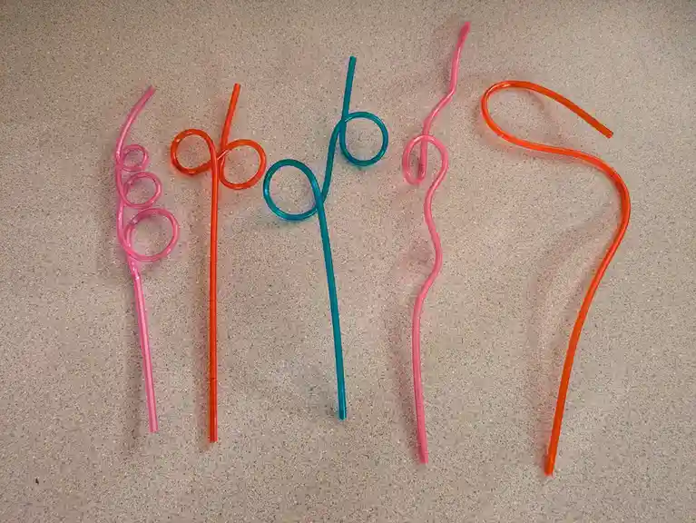 Five colorful plastic drinking straws are arranged on a speckled countertop, each bent into a different shape resembling the…