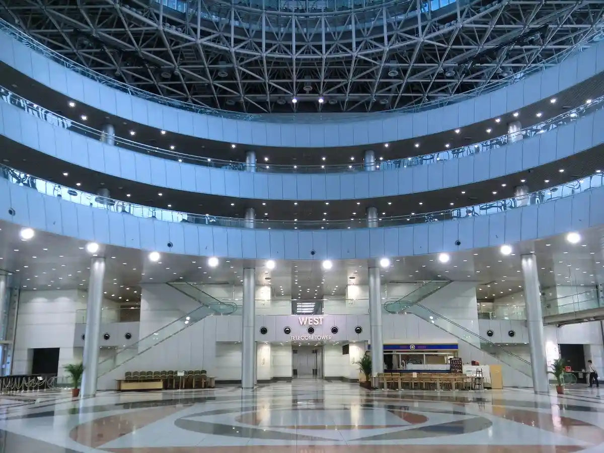 A wide-angle photo of a modern, multi-level atrium with glass railings, escalators, and a high ceiling with exposed metal…