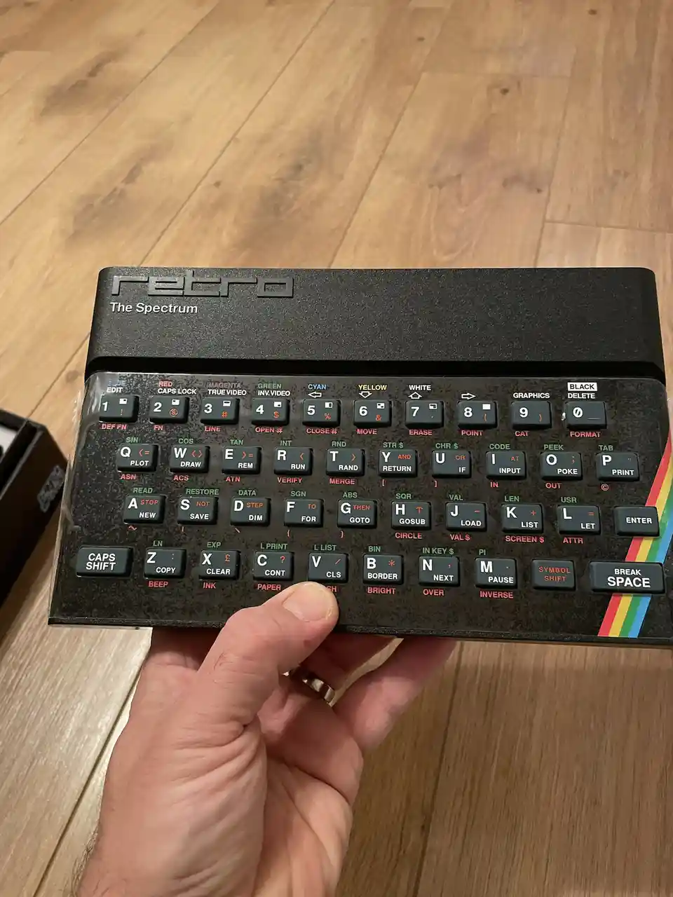 A hand holds a black retro computer keyboard labeled 'retro The Spectrum' with colorful rainbow stripes on the right side…