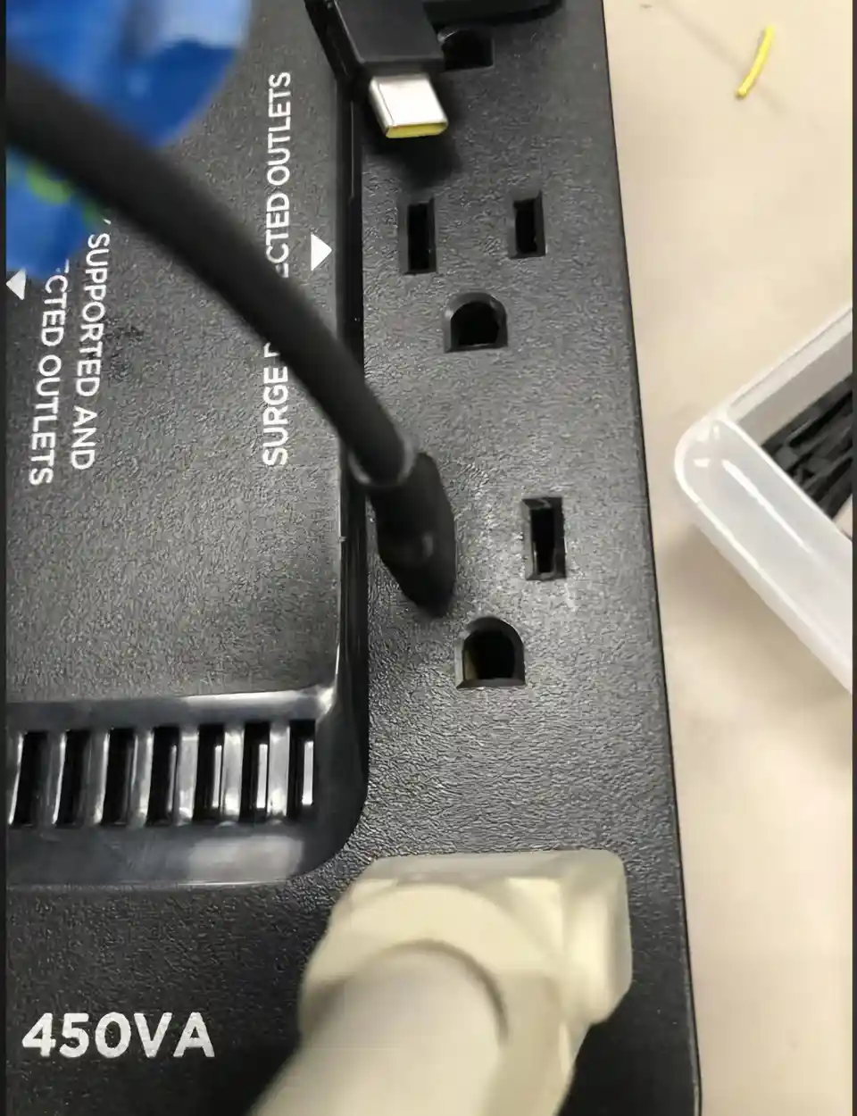 A close-up photo shows a black USB-C cable plugged into a black surge protector, which has multiple electrical outlets. The…
