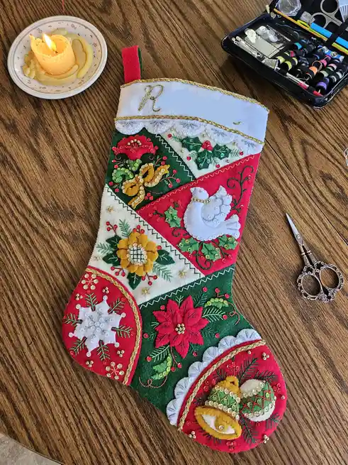 A heavily decorated, hand-embroidered Christmas stocking with red, green, and white felt sections, adorned with sequins…