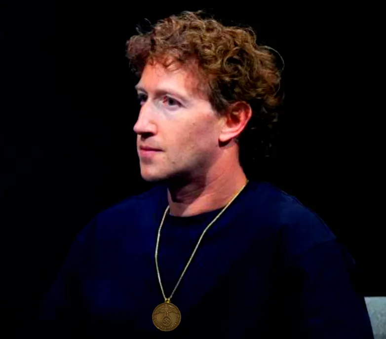 a side profile photo of a man with curly brown hair wearing a dark blue shirt and a gold pendant necklace against a black…