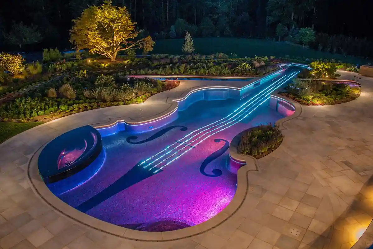 An aerial night photo shows a luxurious swimming pool meticulously shaped like a violin, complete with glowing blue and…