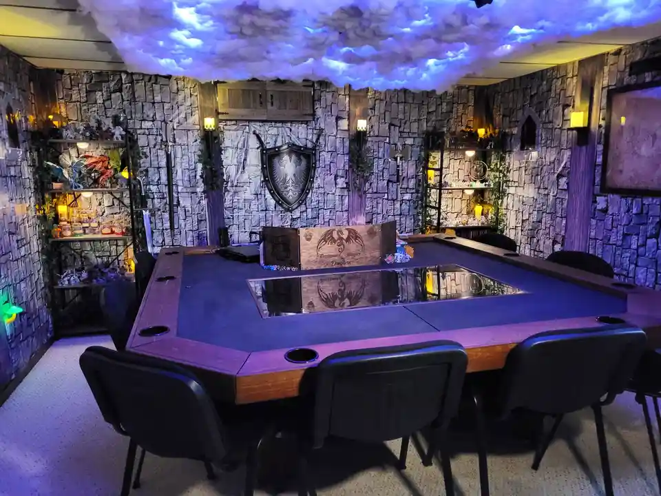 A room decorated like a medieval fantasy dungeon with stone walls, a faux cloud ceiling lit with blue light, and shelves of…