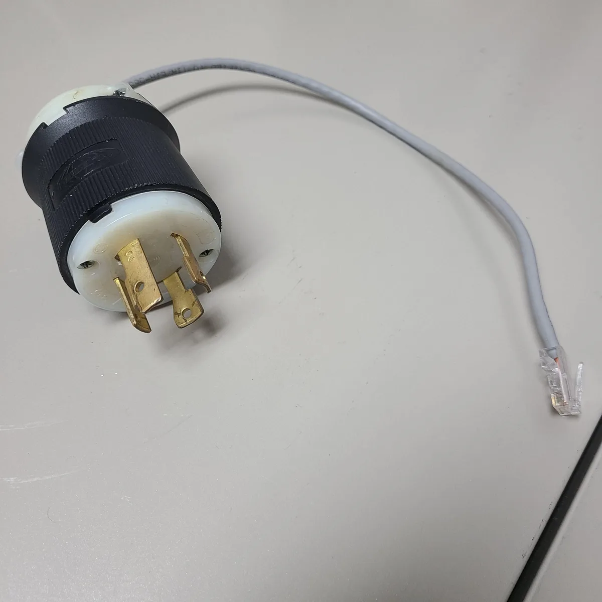 A close-up photo shows a standard US-style electrical plug with a white and black plastic housing and brass prongs…