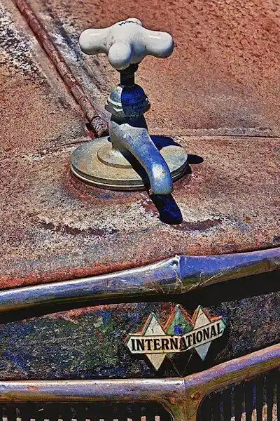 A close-up photo of a vintage, rusted car hood featuring a faucet mounted on the surface, with the 'INTERNATIONAL' brand…