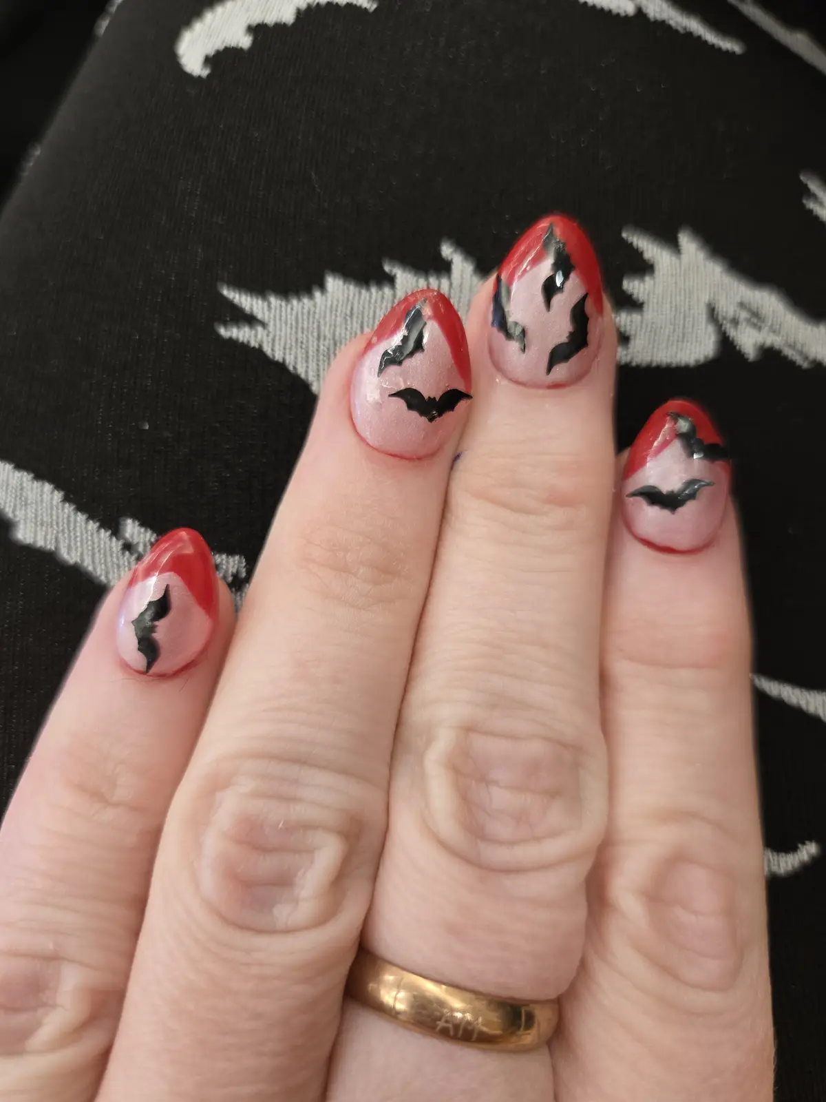 A close-up of a person's hand showing four fingernails with Halloween-themed nail art; each nail has a red-tipped design…