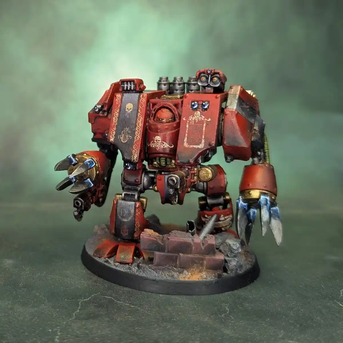 A heavily detailed, red and black painted miniature of a humanoid robot or war machine with skull motifs, standing on a base…