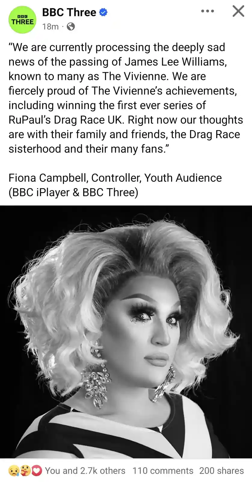 A black-and-white portrait of drag queen The Vivienne, featuring her voluminous blonde wig, dramatic makeup with glittery…