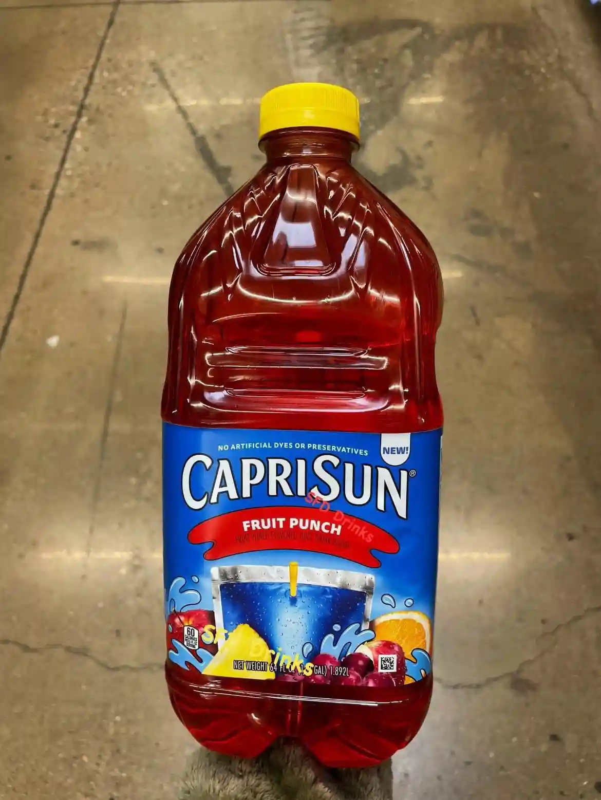 A large, 64-ounce plastic bottle of Capri Sun Fruit Punch sits upright on a concrete floor, its red liquid visible through…