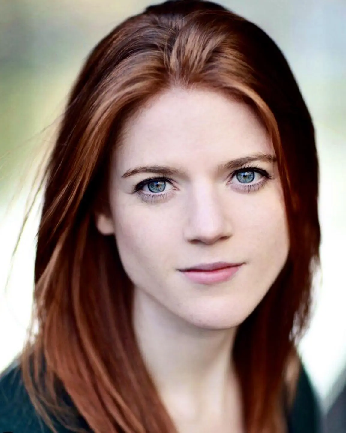 A close-up portrait of a woman with red hair and blue eyes, looking directly at the camera with a neutral expression. The…